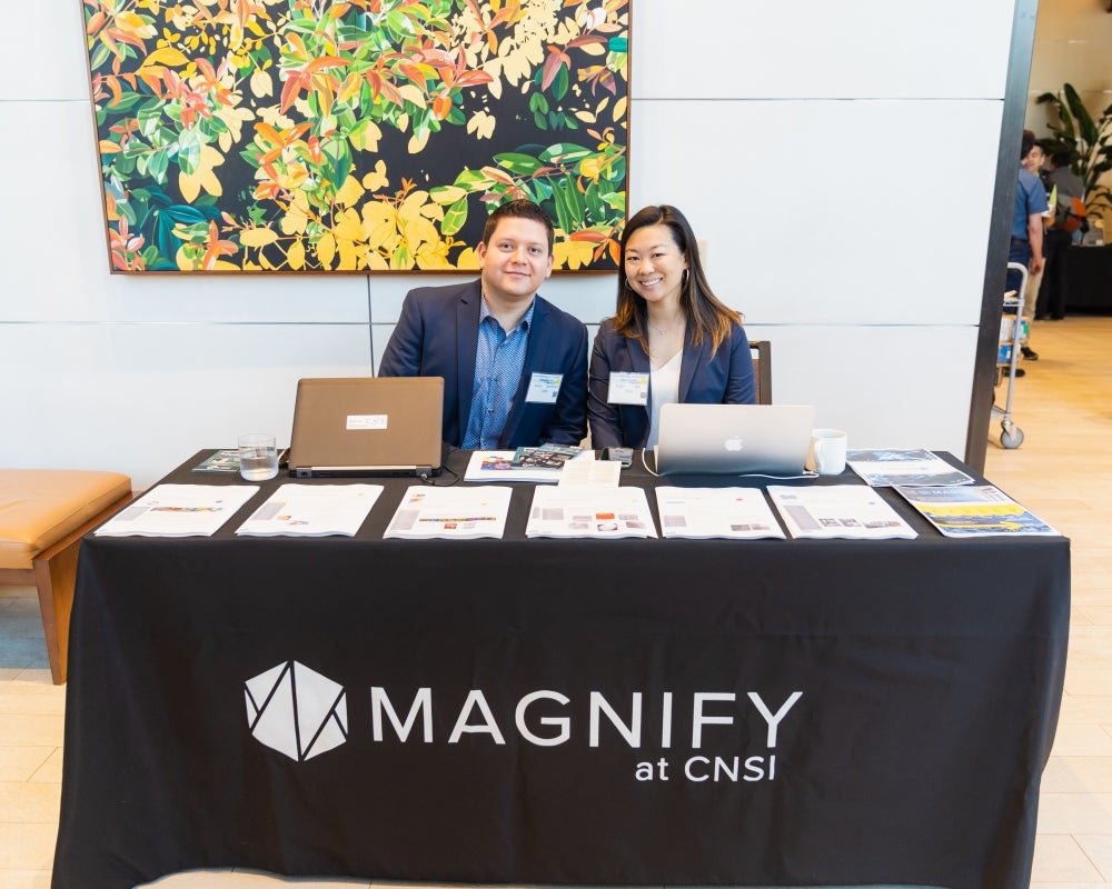 A smiling man and woman seated at the Magnify at CNSI Exhibitor Table