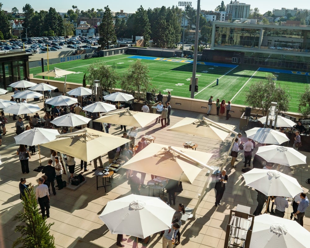 Overhead view of a sunny outdoor terrace with several shade umbrellas and a crowd of attendees networking