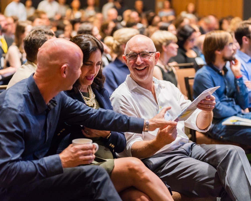 Three attendees chatting and laughing as they look over the program brochure