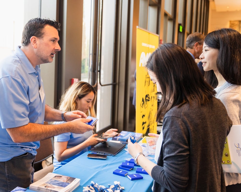A man working at an exhibitor table talking to two young women