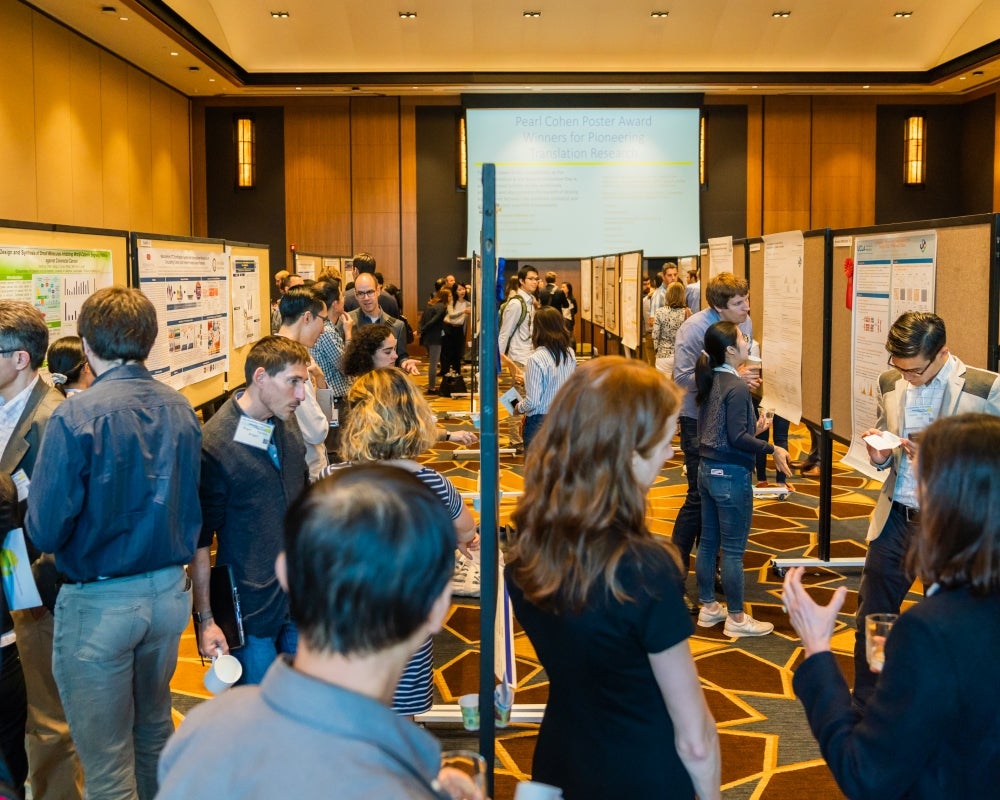 A large hall with rows of information posters and a crowd of attendees reading them