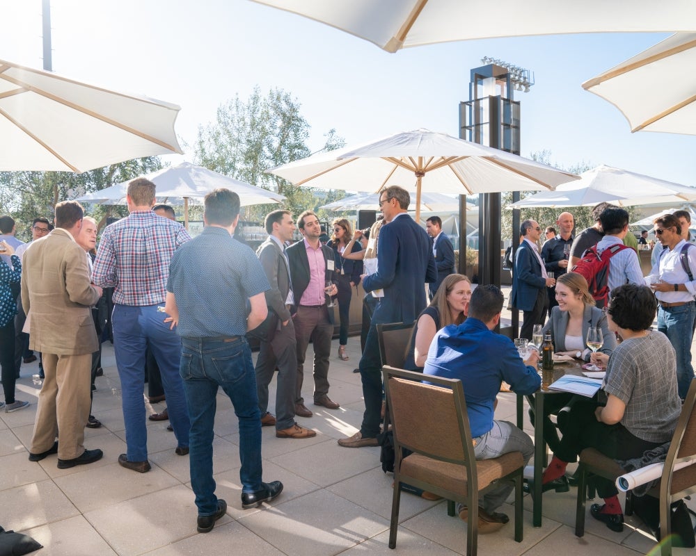 Attendees casually mingling outdoors under shade umbrellas